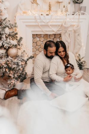Family holiday photo with Christmas decorations, white fireplace, and cozy winter outfits.