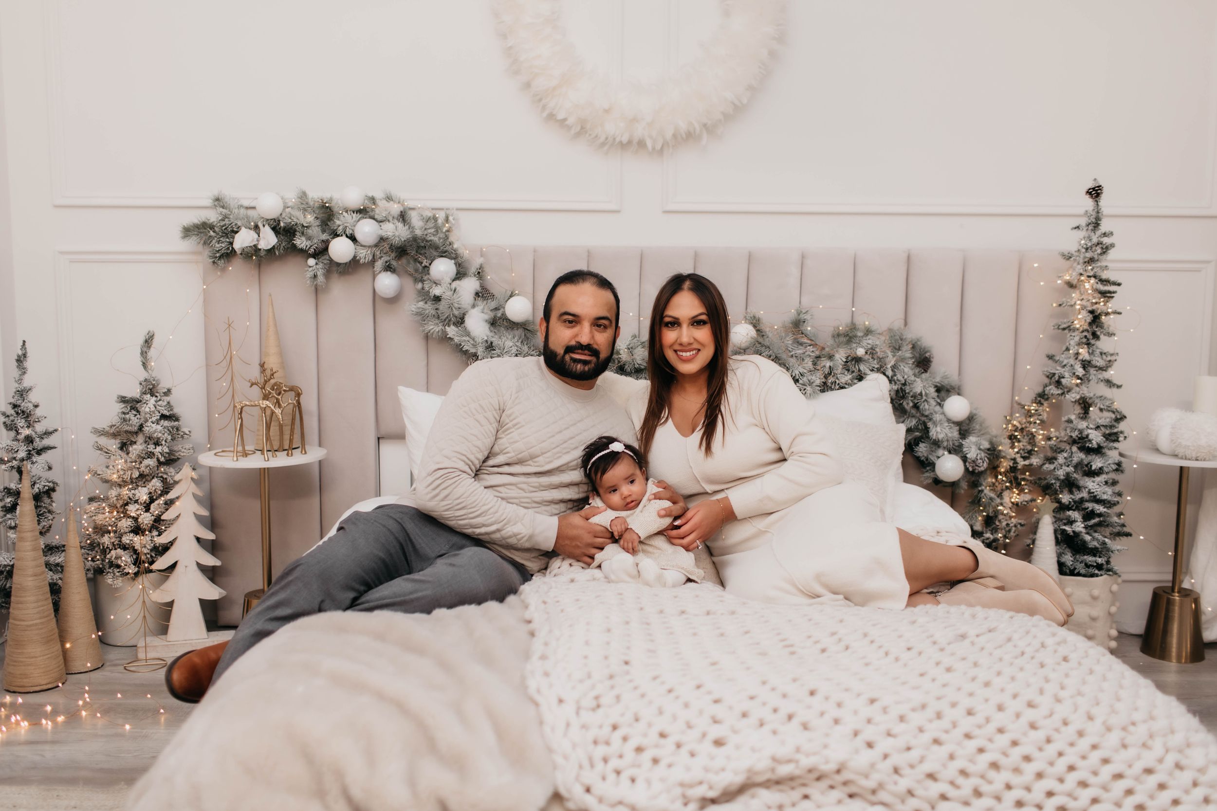 A family sits together on a bed decorated with winter holiday decor and white bedding.
