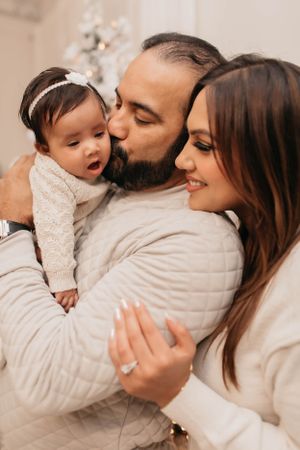 A tender family moment captured in warm tones as they share affection with their baby in white.
