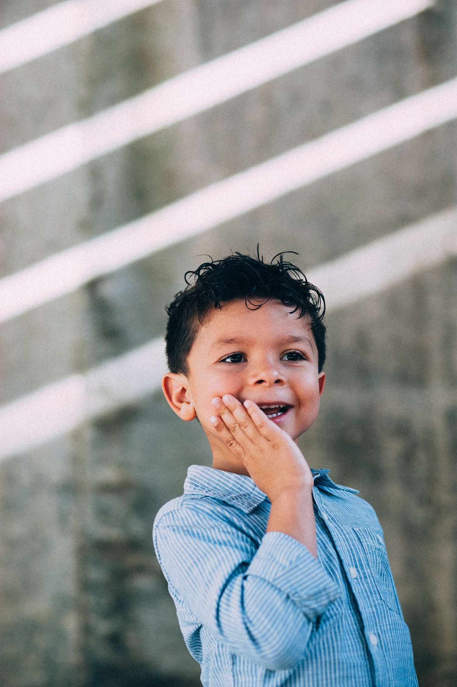 A young child laughs and holds their cheek against a striped background.