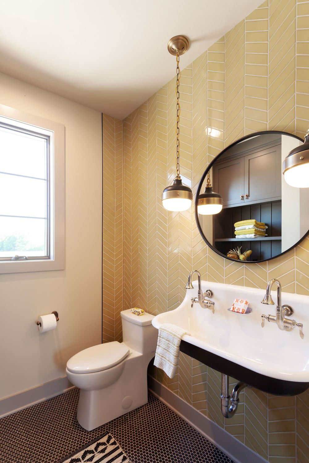 Modern bathroom with geometric wallpaper, round mirror, and pendant lighting.