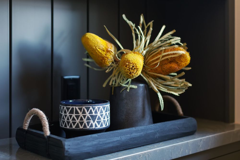 Artistic still life with yellow flowers in black vase beside patterned container.