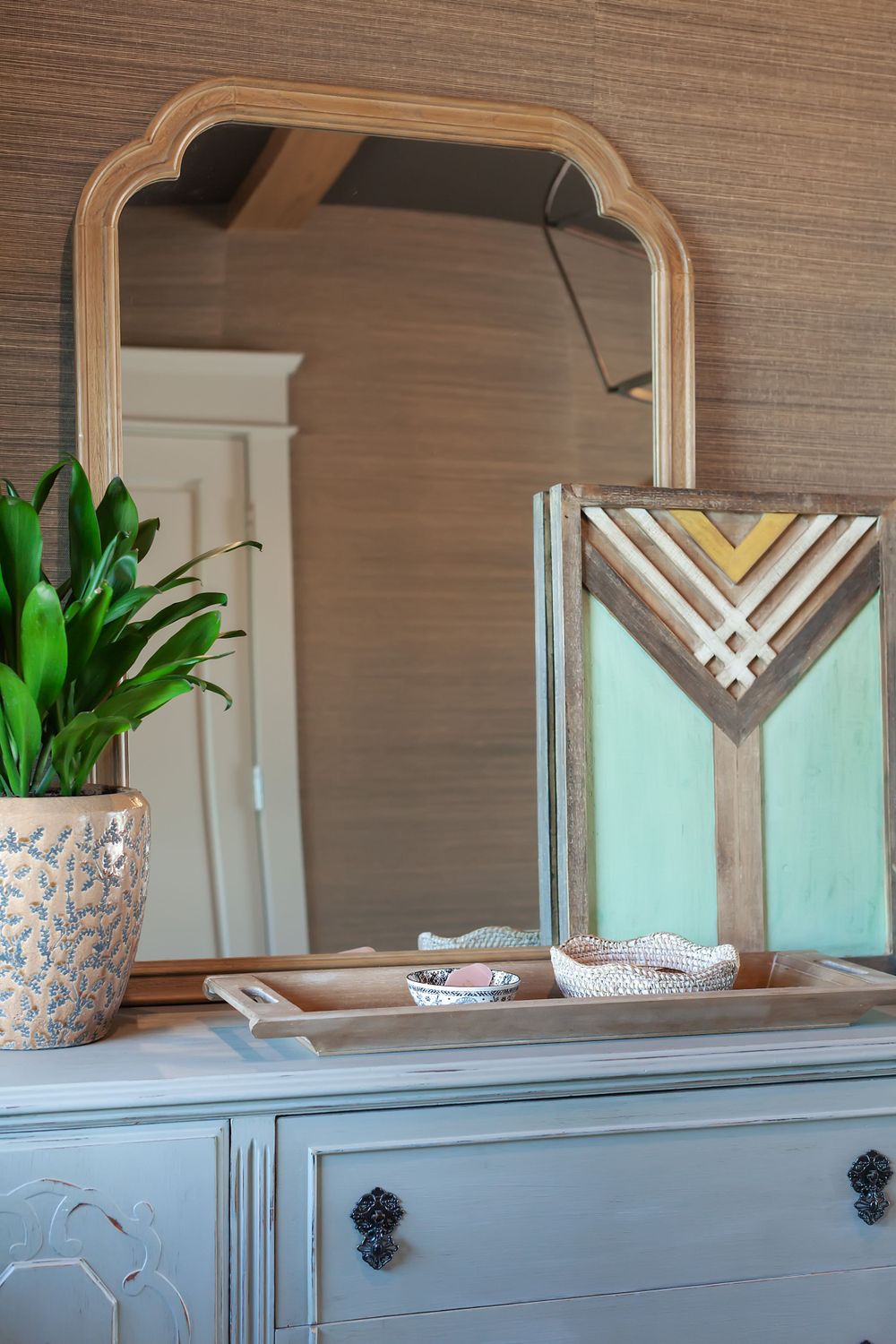 Vintage dresser with arched mirror and decorative items styled with potted plant.