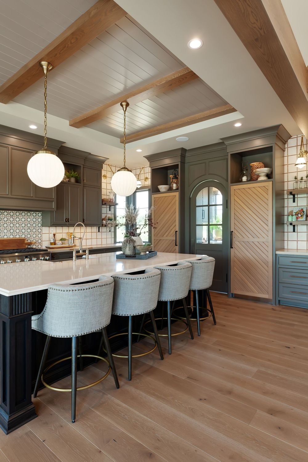 Elegant kitchen island with upholstered bar stools, globe pendant lights and wood beam ceiling accents.