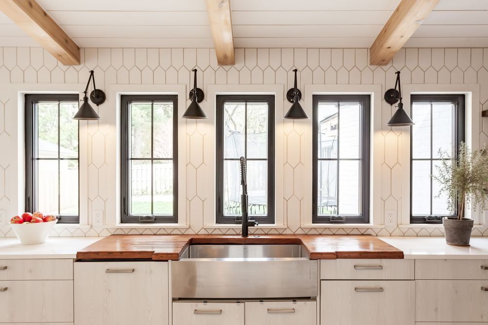 Open concept kitchen with exposed beams, black lighting fixtures, and white brick walls.