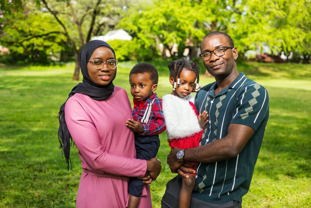 Happy family of four poses together in casual attire against lush garden background.