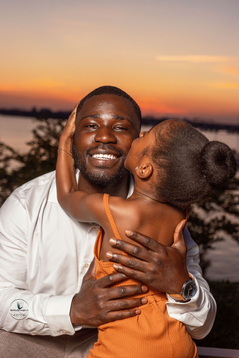 An intimate sunset portrait capturing a tender moment against an orange sky.