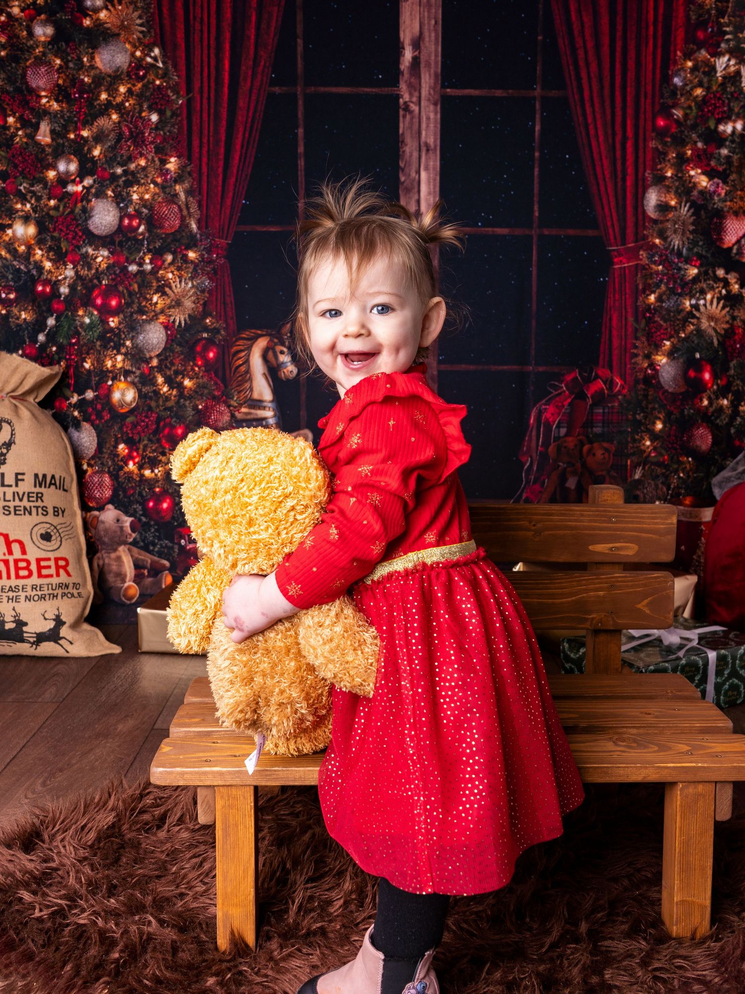Toddler girl smiling in red dress with teddy bear at christmas session in Doncaster client of Heather Katie Photography.