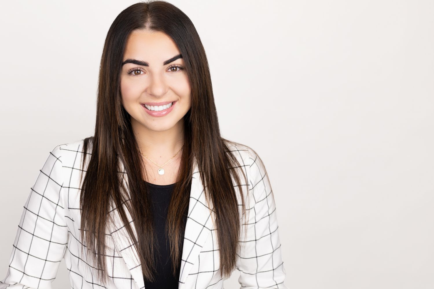 Professional headshot of person in black and white checkered blazer against white background.