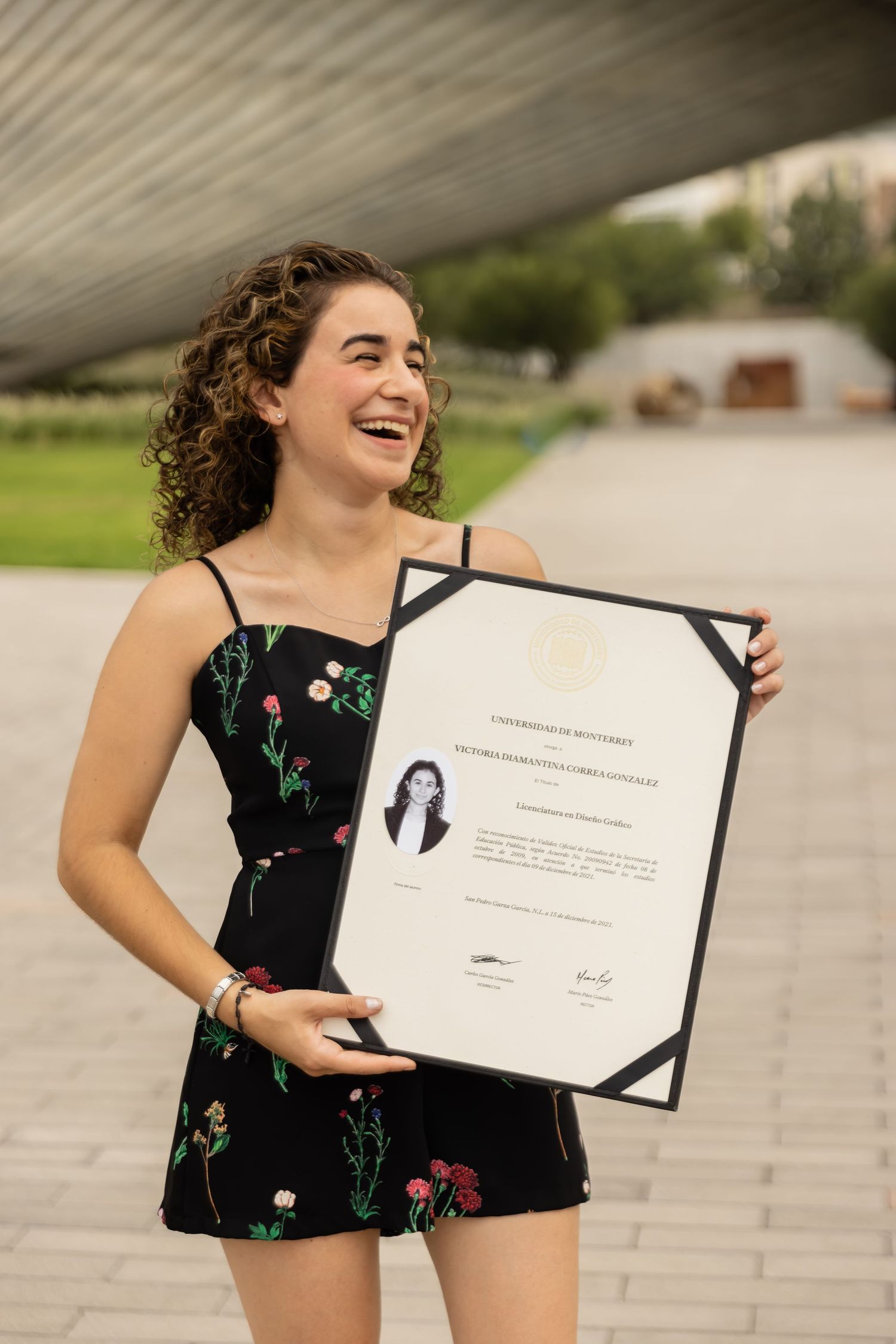 Smiling young woman holding a university diploma certificate outdoors at graduation.