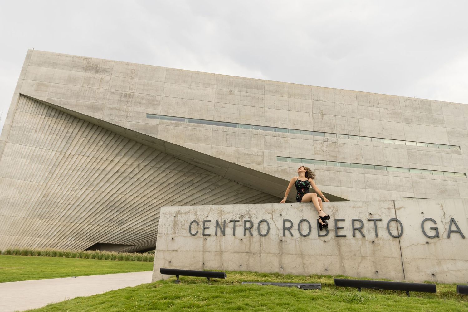 Woman sitting on Centro Roberto Garza Sada concrete building sign outdoors.