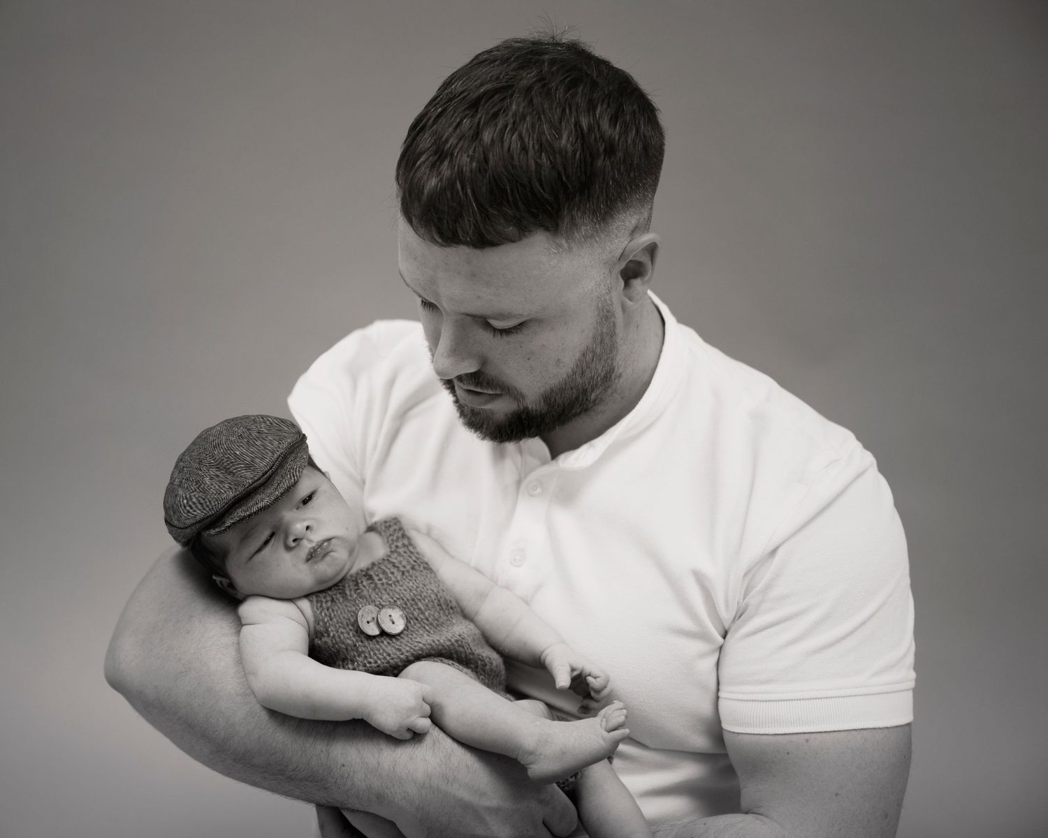 Newborn family shoot, Black & White image dad in white polo, baby wearing grey tween cap & grey knitted outfit