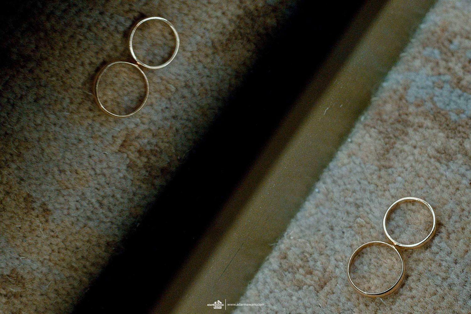 Two pairs of golden wedding rings captured on a textured surface with moody lighting.