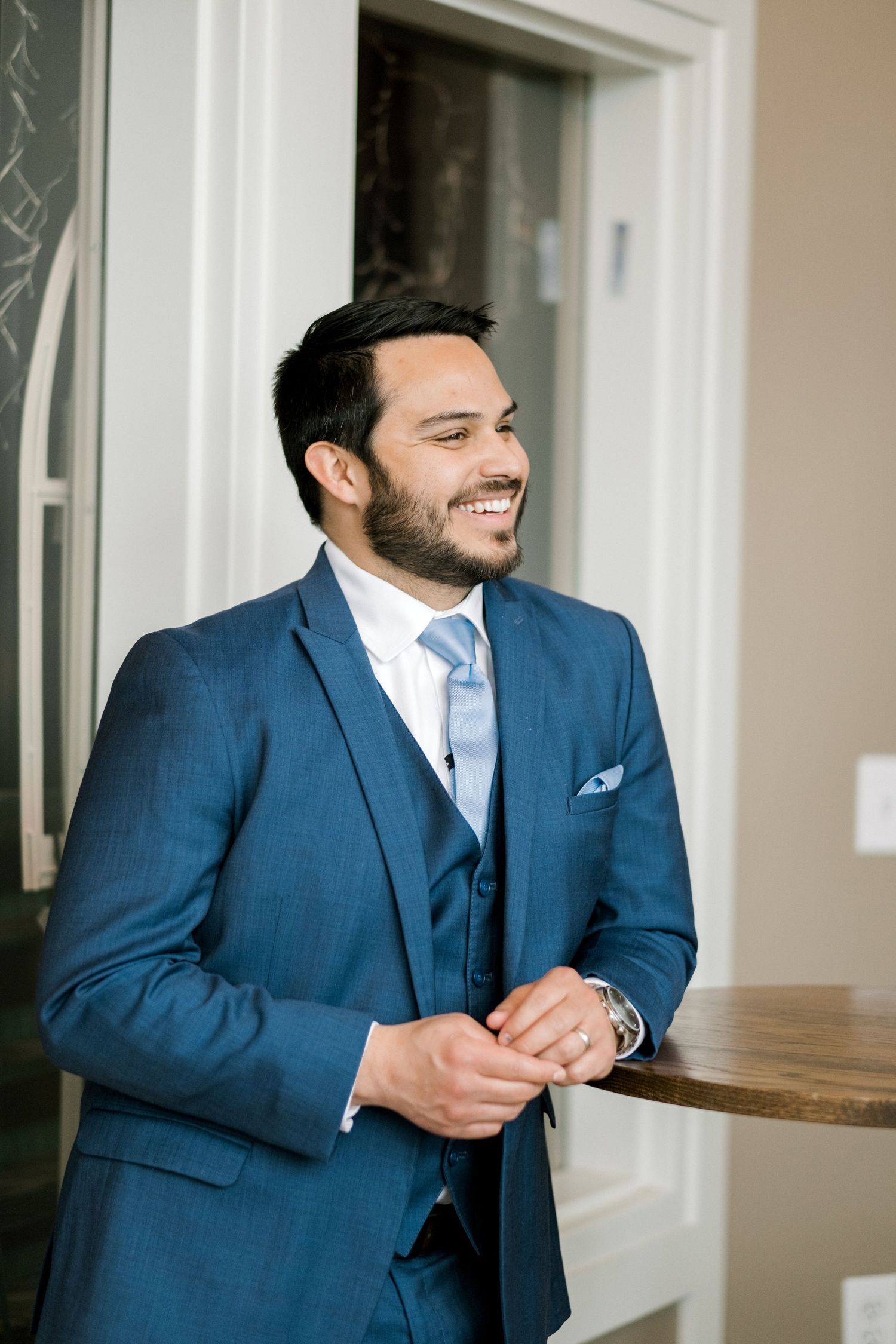 A well-dressed person in a navy blue three-piece suit smiling warmly during a formal event.