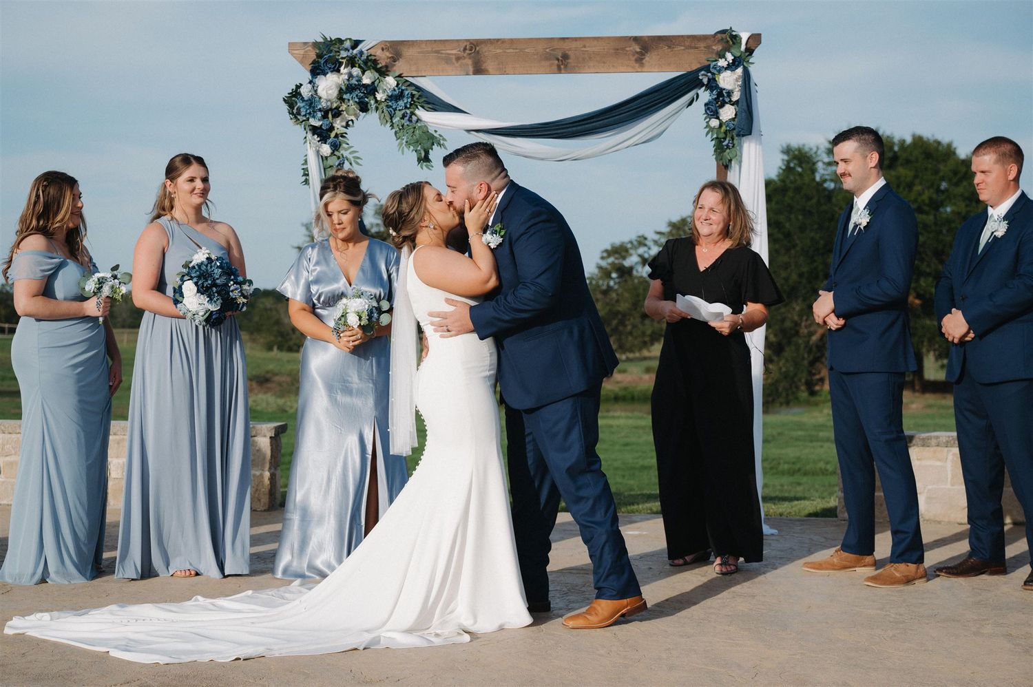 A wedding ceremony with attendants in gray dresses under a decorated arch.