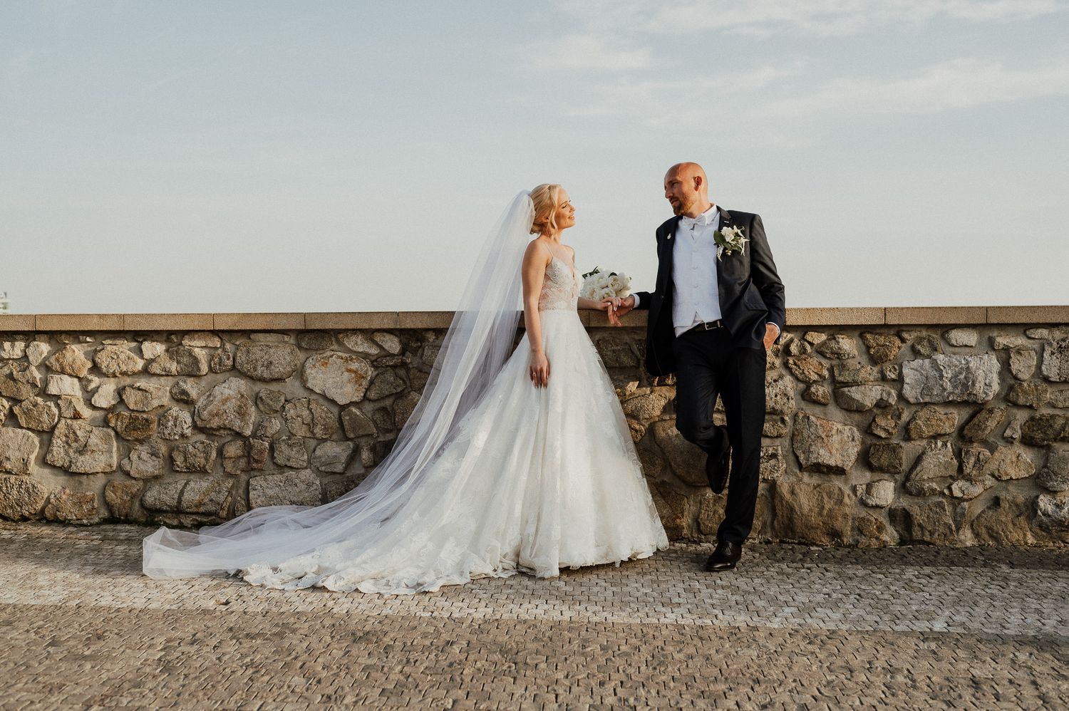 Wedding couple posing against stone wall during golden hour portrait session.