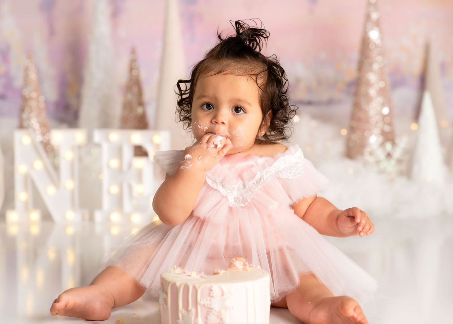 smash cake winter onderland, where a baby puts her hand to her mouth while covered in cake