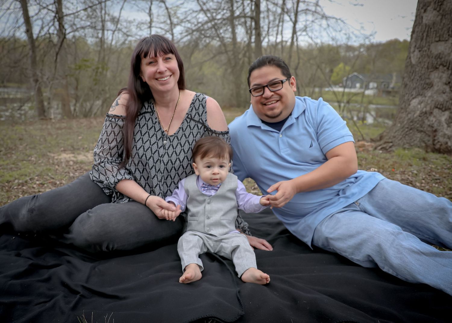 A family relaxes together on a black blanket during an outdoor photo session. Family photoshoot. L. Visions Photography.