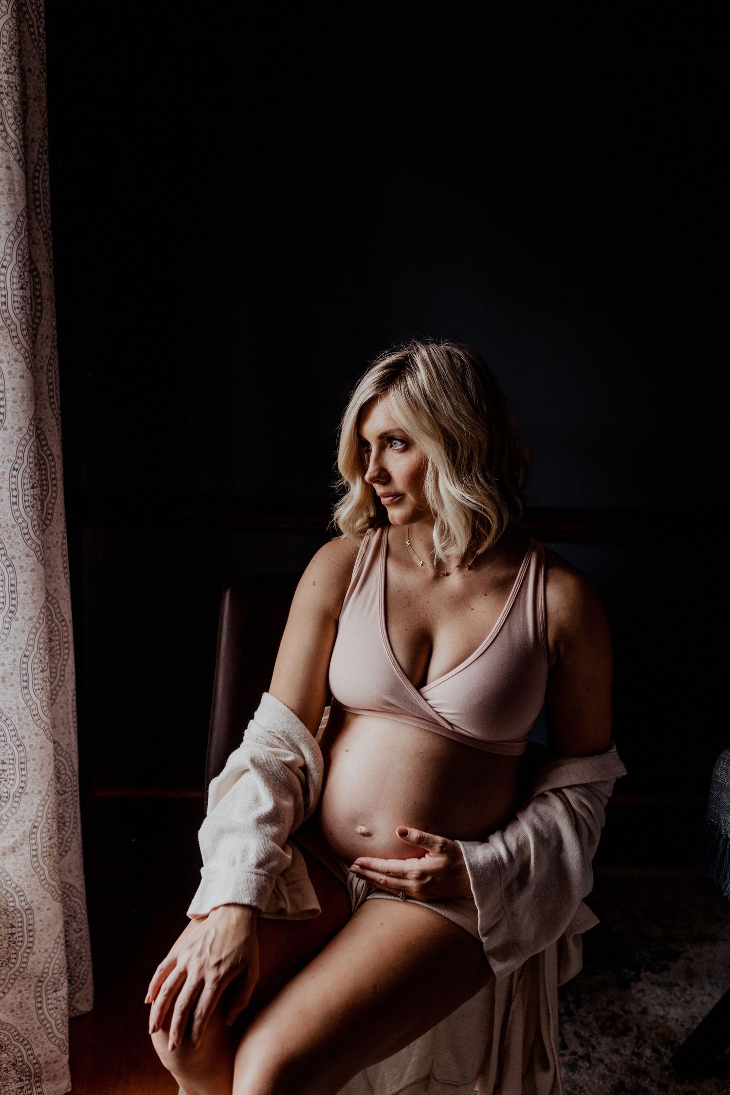 pregnant woman sitting next to window in her home wearing a satin lounge set