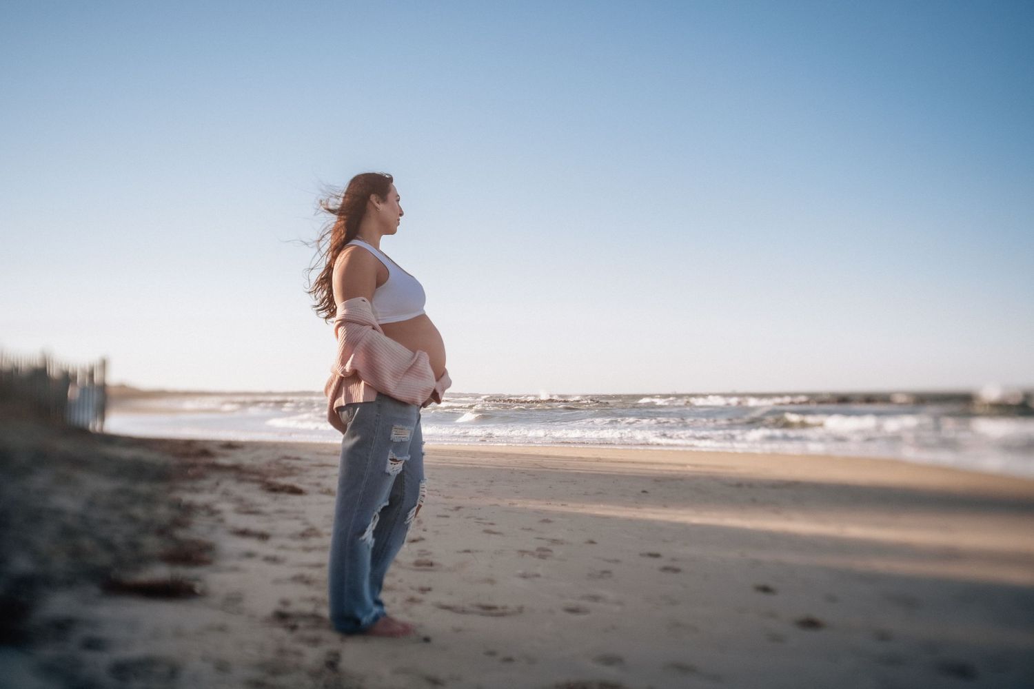 pregnant woman on the beach in norfolk, virginia with wind blowing and bare belly