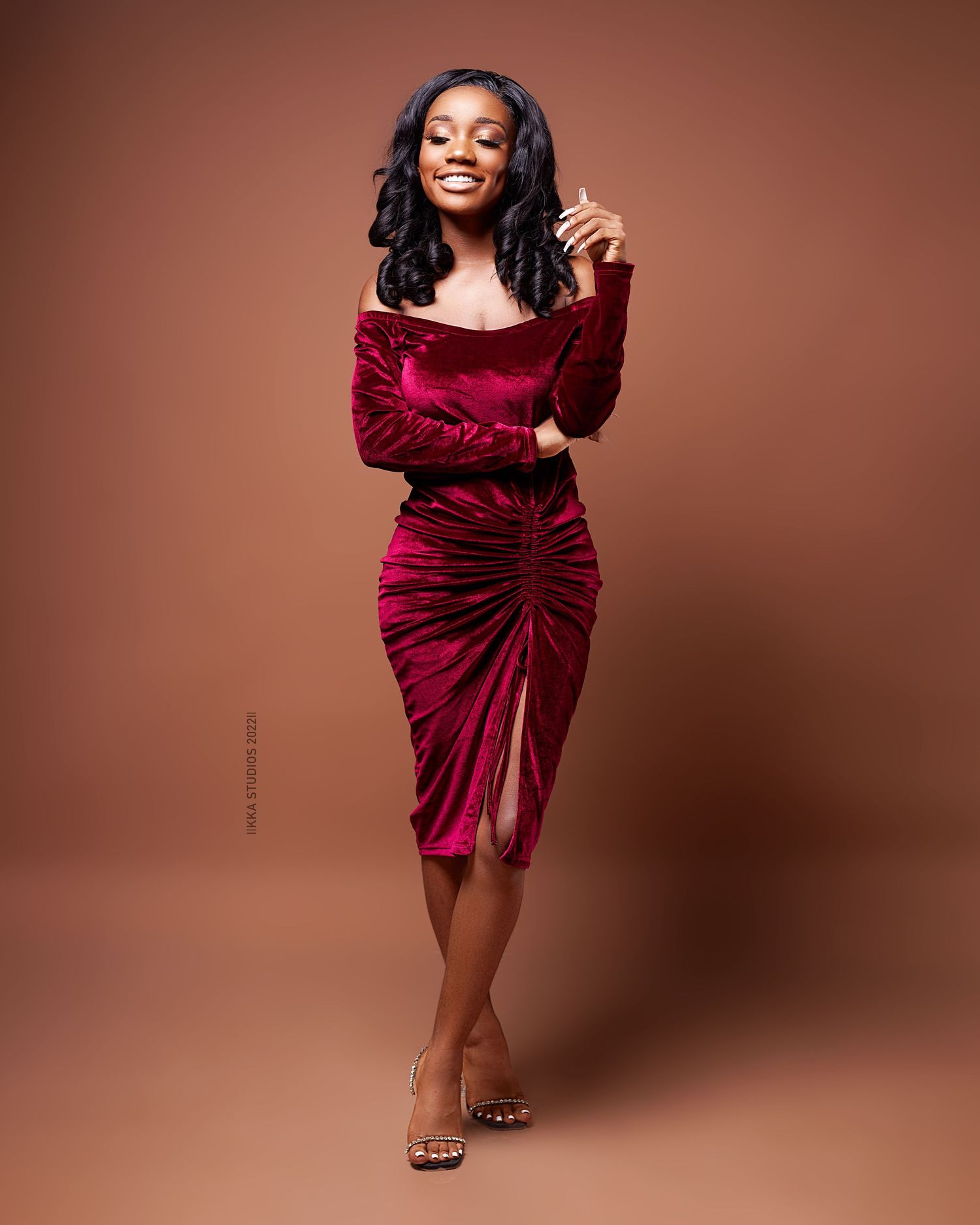 Glamour photoshoot featuring a burgundy velvet dress against a warm brown background.