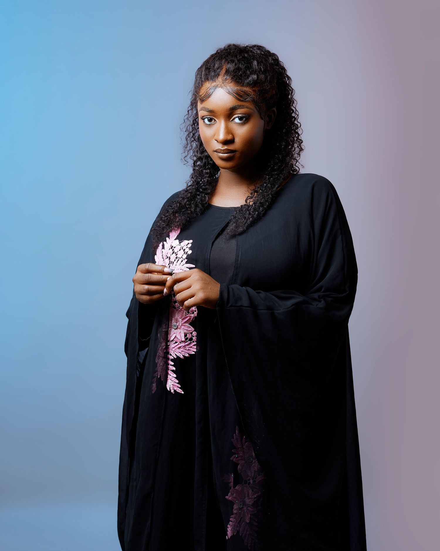 Figure in flowing black robe poses dramatically against gradient blue background.