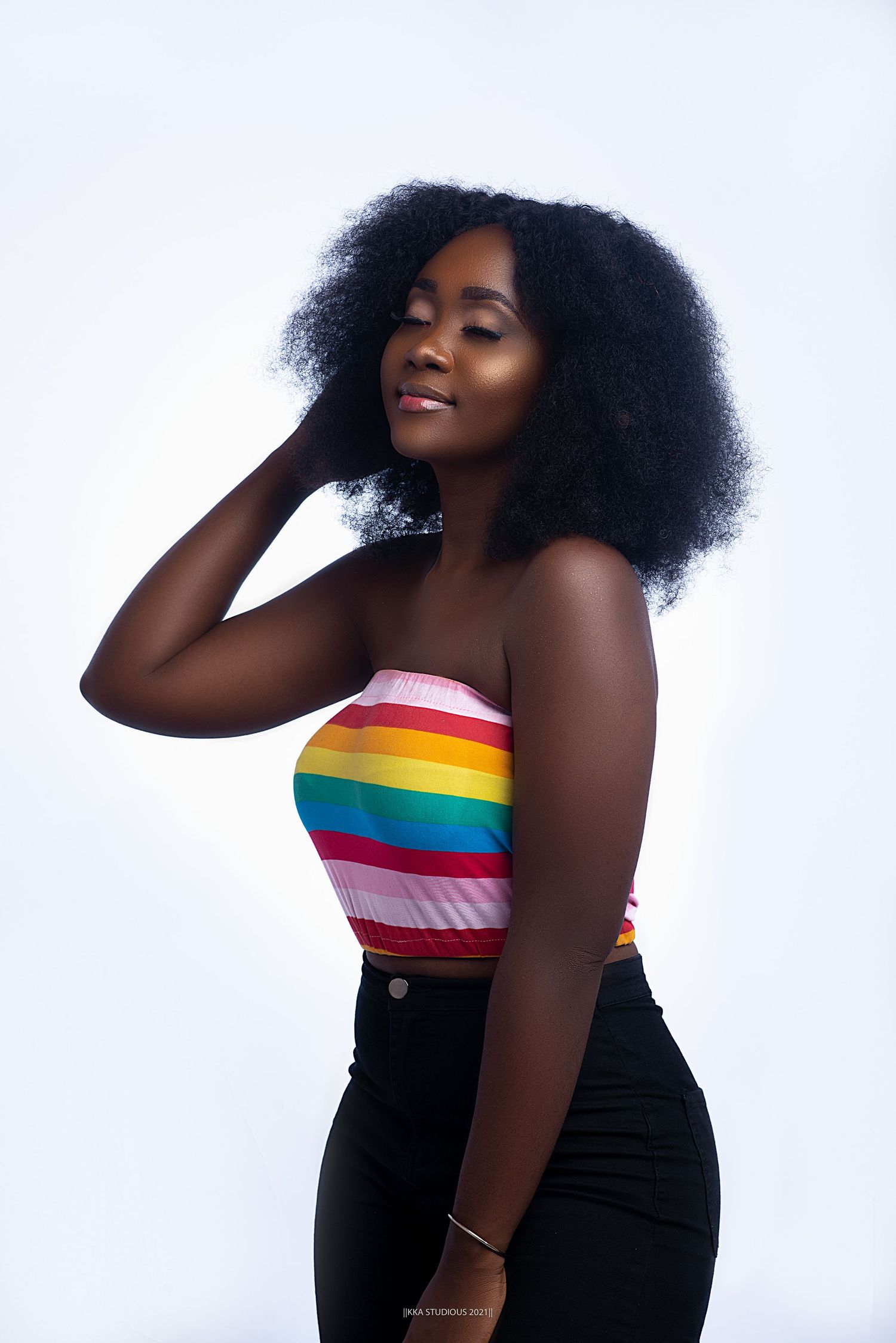 Portrait in rainbow striped top against white background with natural hair styling.