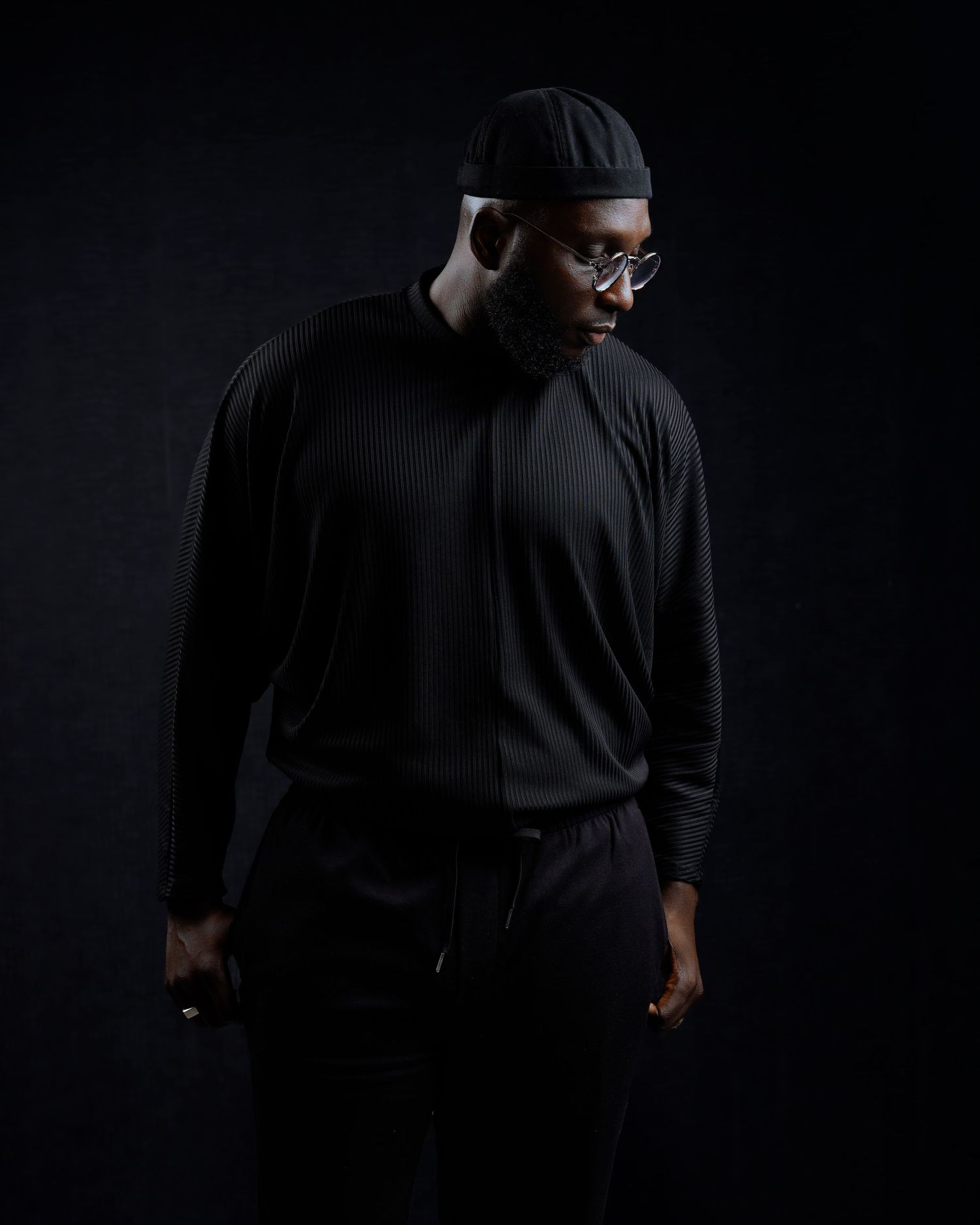 Moody low-key portrait in dark clothing against black background with dramatic side lighting.