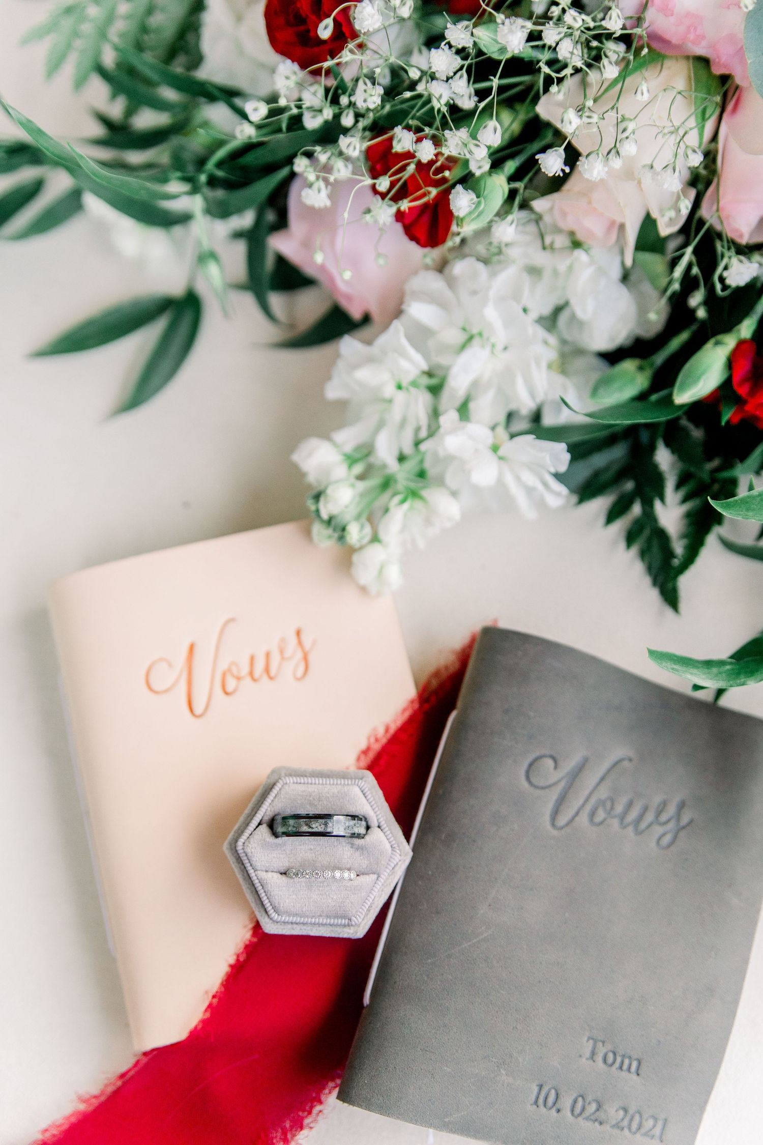 Wedding vow books with floral decor and calligraphy in red and gray.