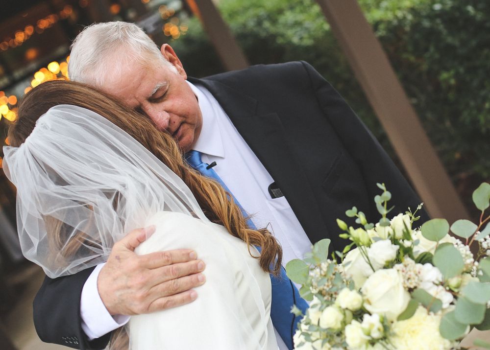 An emotional embrace during a wedding celebration with white floral bouquet.