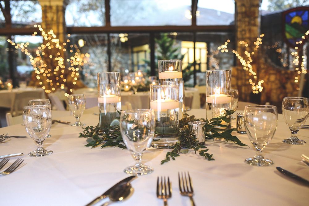 Elegant wedding reception table setting with glowing candles and greenery decorations in an indoor venue at night.