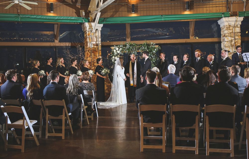 Wedding ceremony in progress at indoor venue with wooden beams and stone pillars.