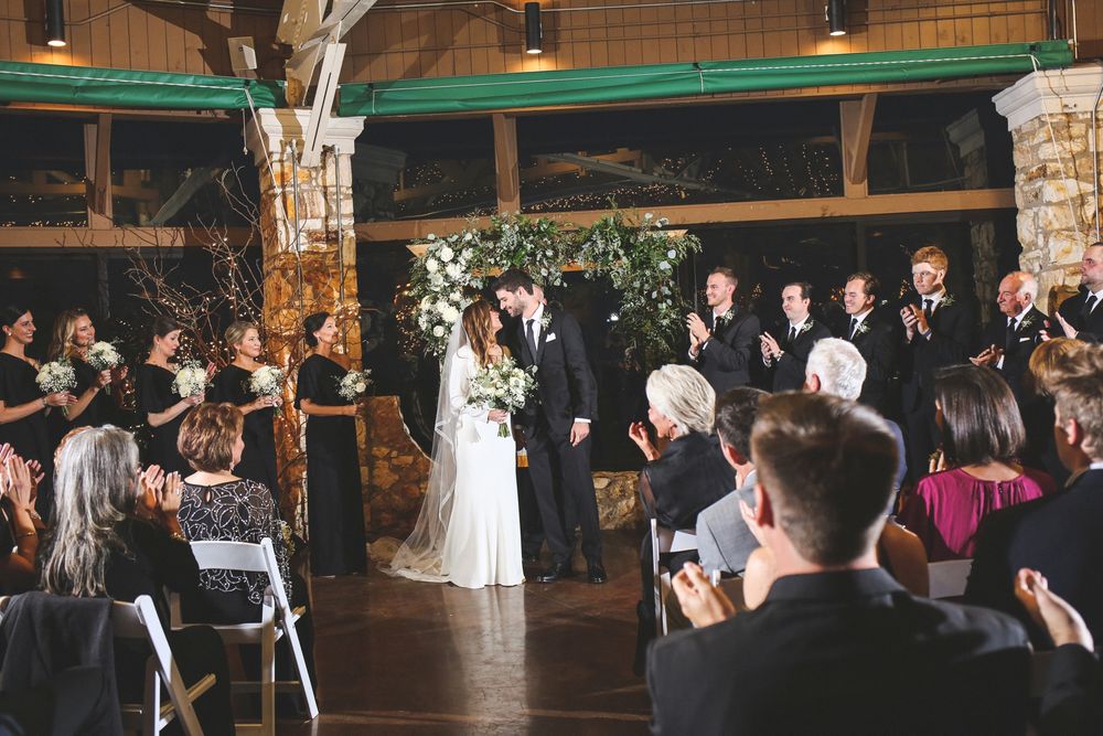 Wide view of wedding ceremony in progress with guests capturing photos on phones.