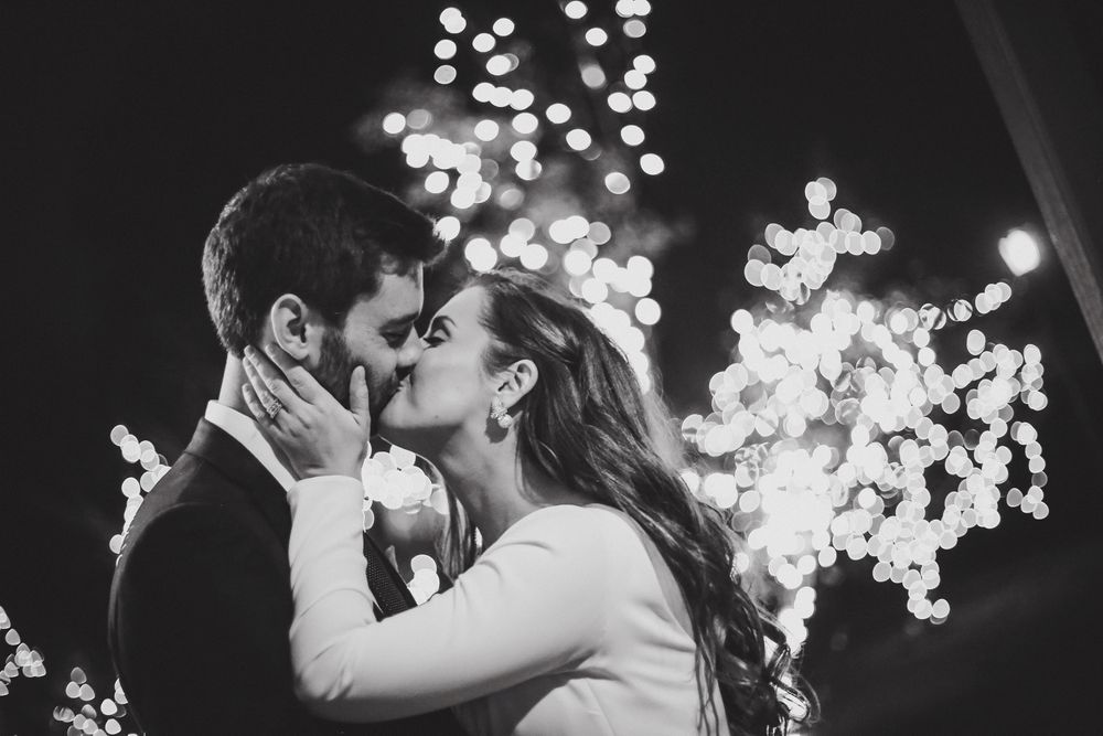 A romantic kiss under twinkling lights captured in black and white photography.