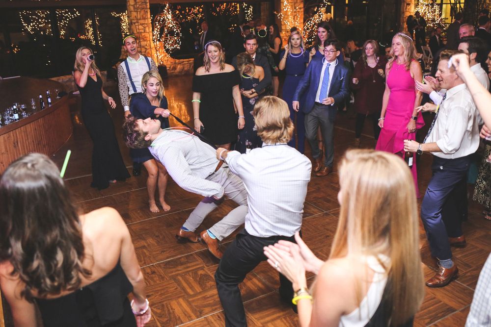 Wedding guests dancing energetically on a wooden dance floor at a reception.