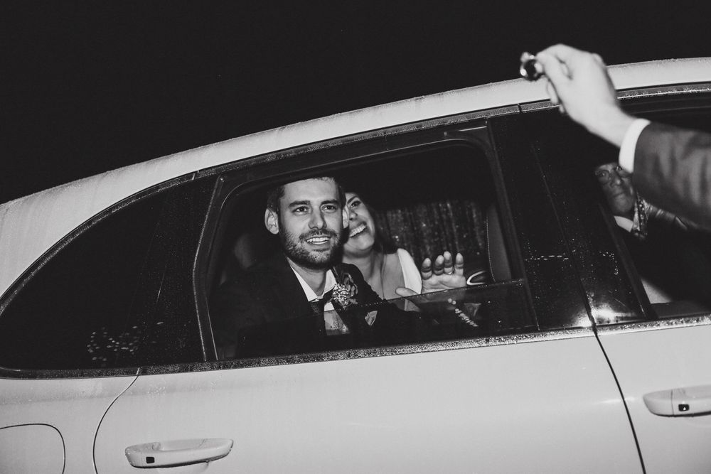 A departing couple smiles through a car window in black and white photography.