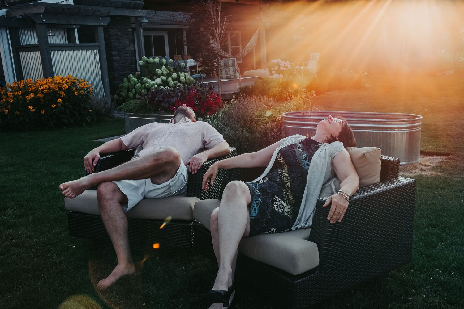 Two people relaxing on outdoor furniture at sunset in a garden.