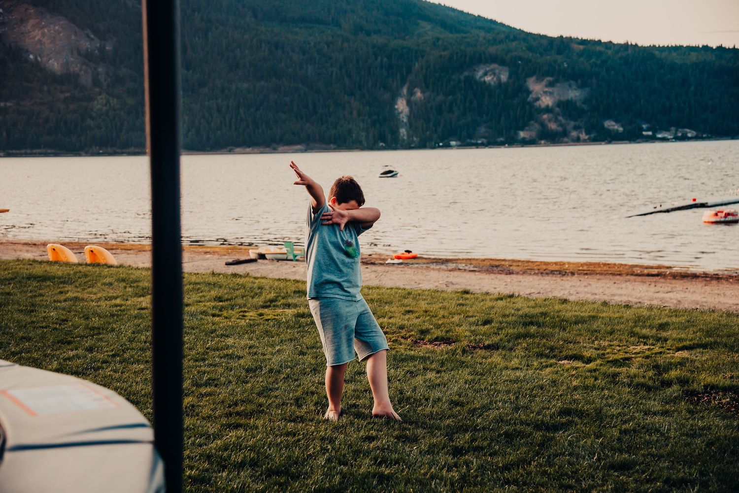 Child playing outdoors near a lake with mountains in background.