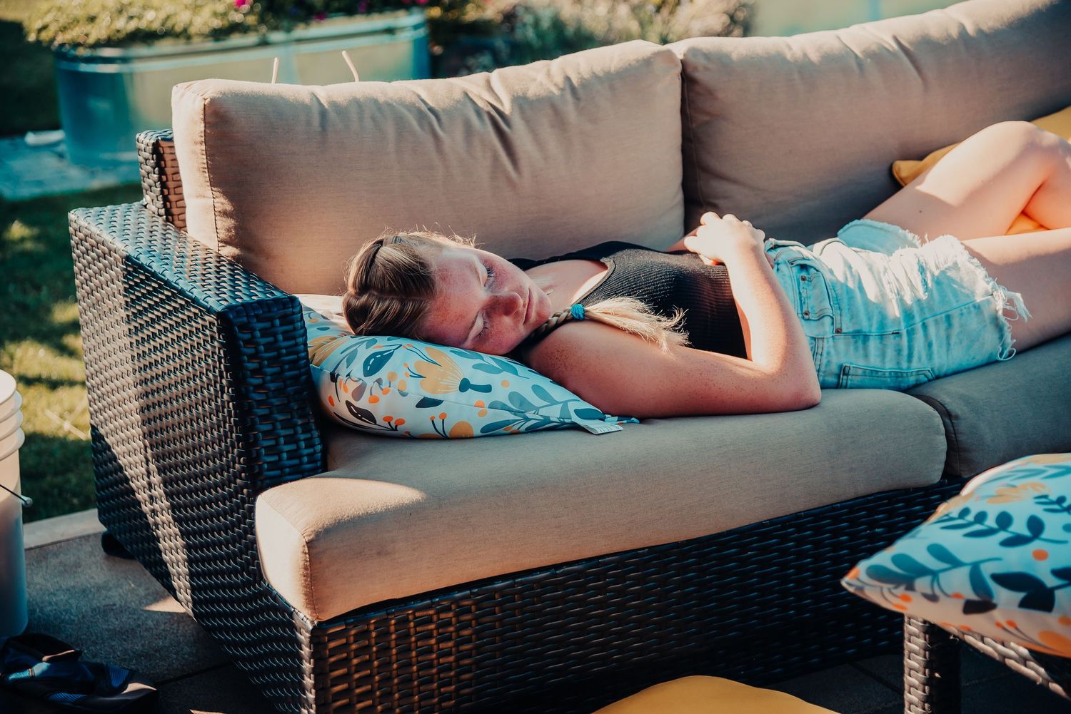 Someone napping peacefully on an outdoor wicker couch with cushions.