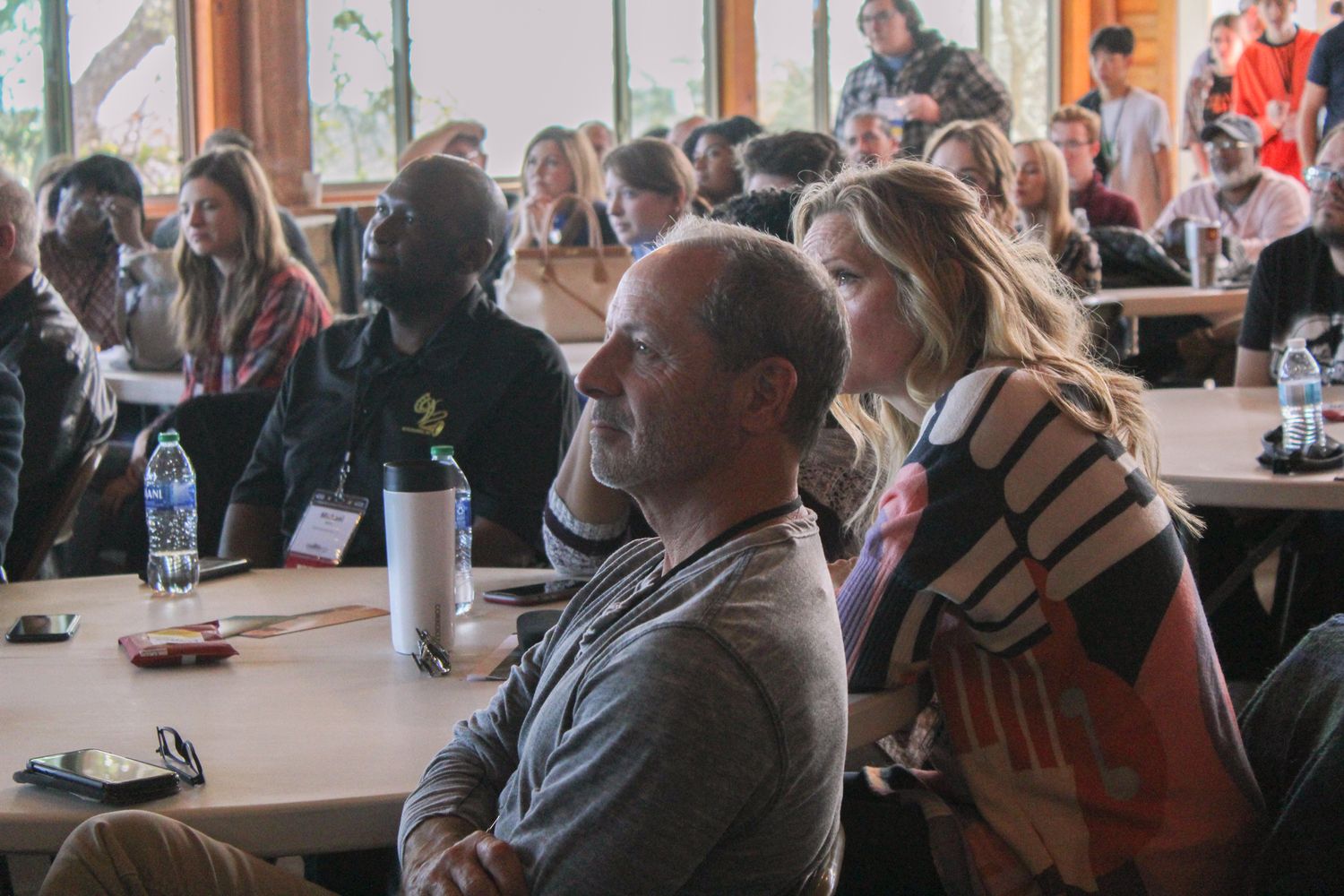 Diverse group of adults seated at round tables during an indoor conference event.
