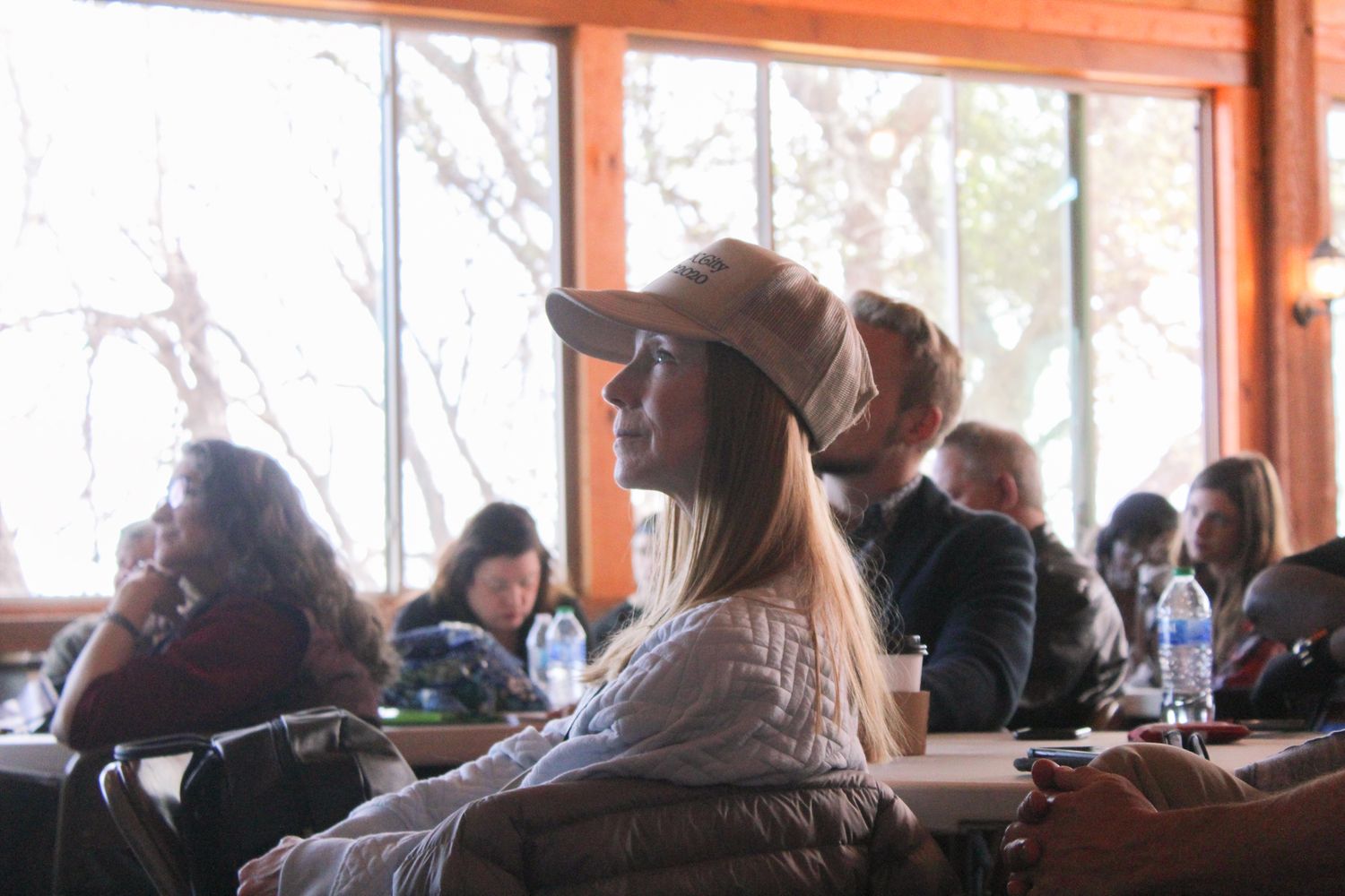 A woman wearing a tan cap listens attentively during an indoor event at a wooden venue.