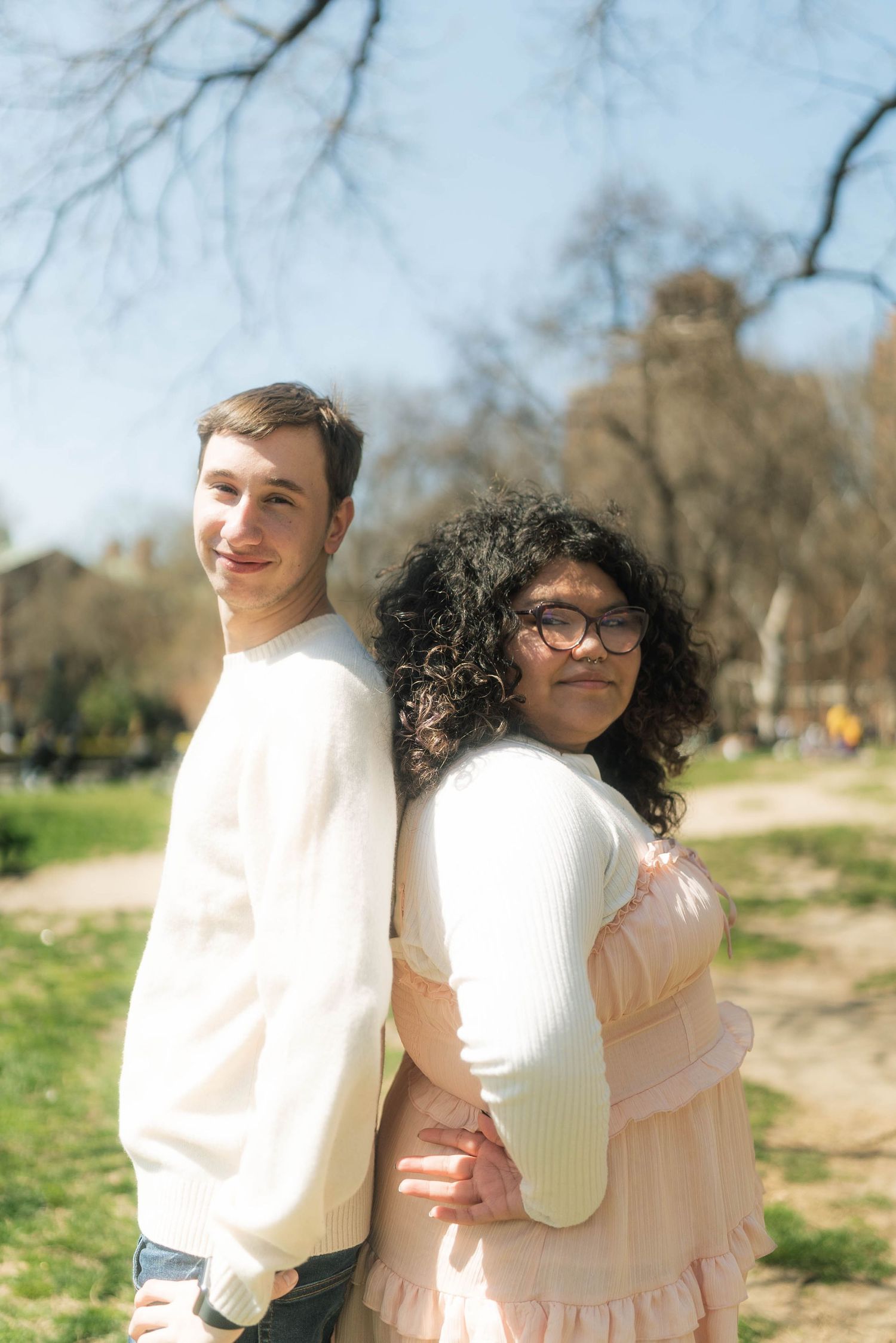 Couple in light colored outfits embrace while standing in sunny outdoor setting.