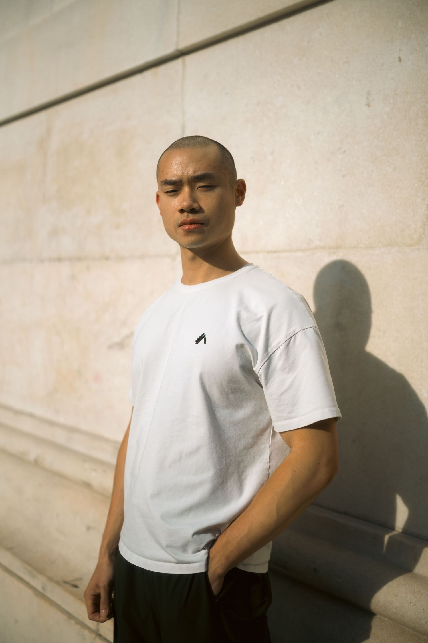 Minimalist portrait series against white wall featuring white t-shirt and dramatic shadows.