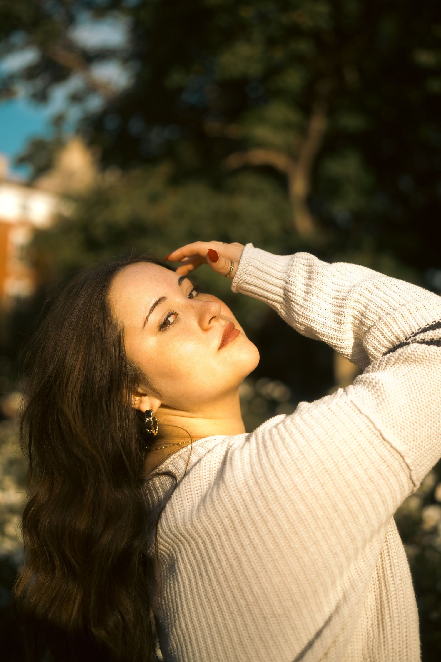 Person in cream sweater poses with dramatic lighting in natural setting.