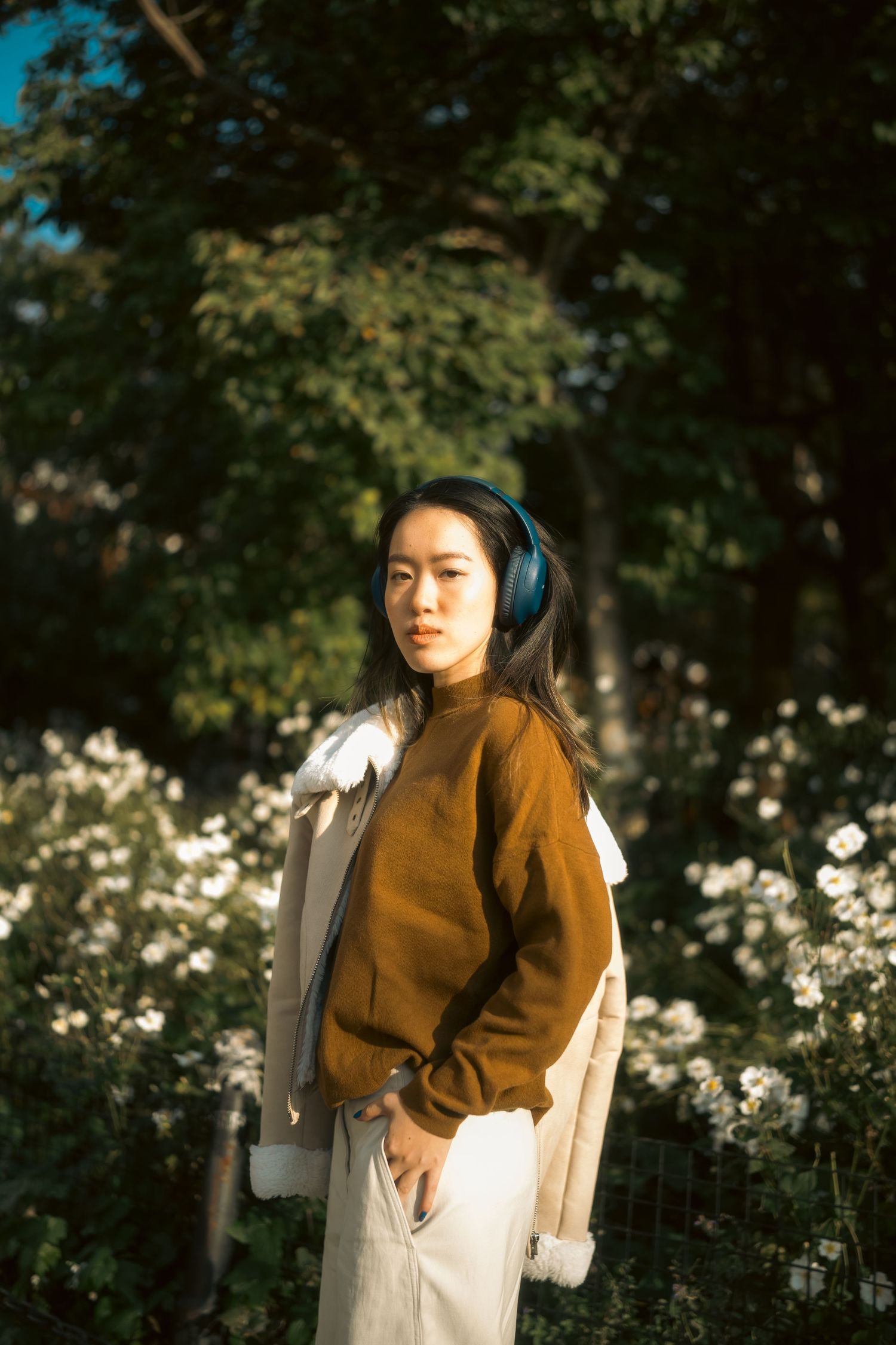 Autumn fashion shoot featuring brown hoodie and backpack among garden foliage.