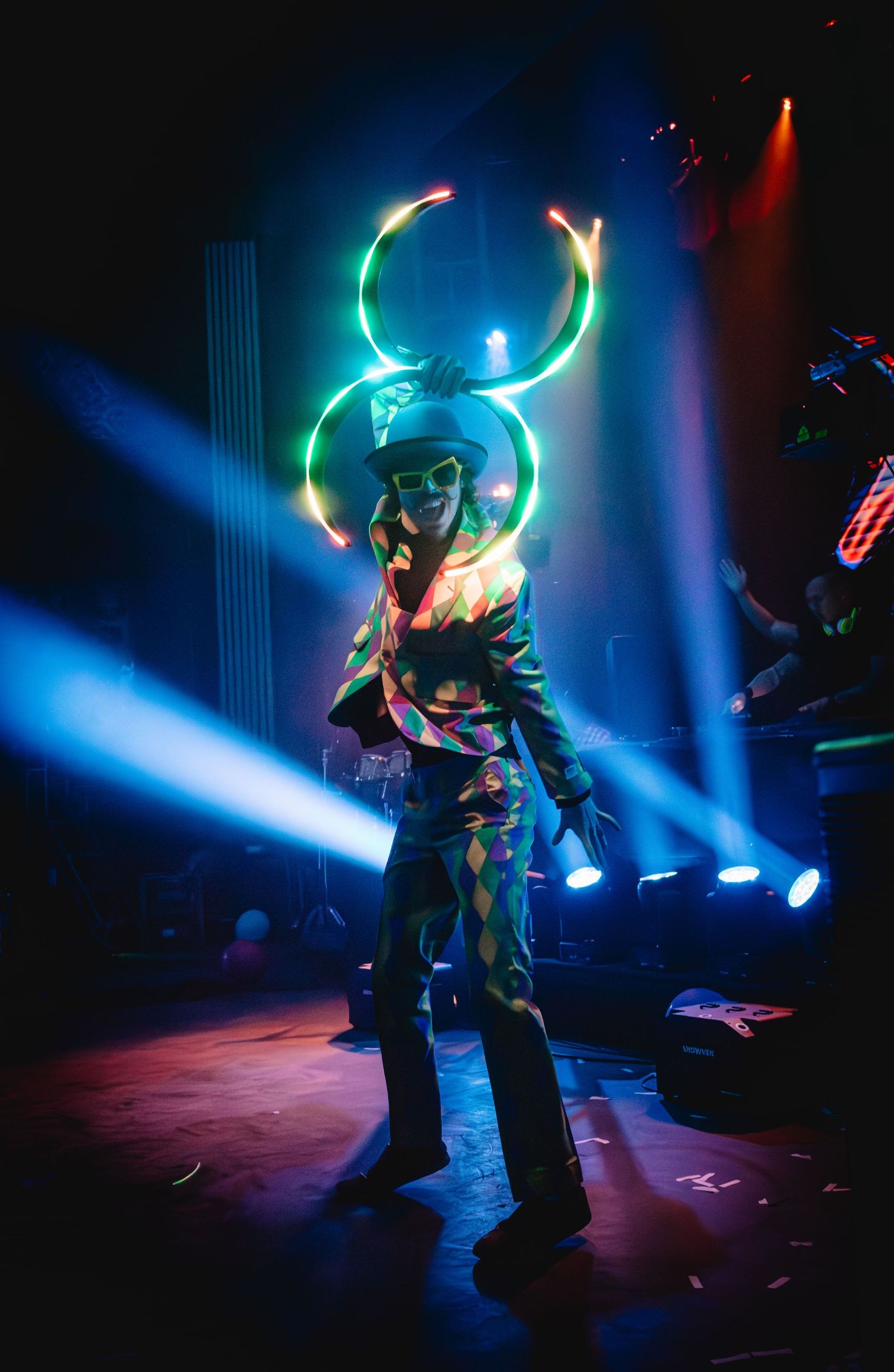 Performer with illuminated neon rings creates a dazzling light show on a dark stage.