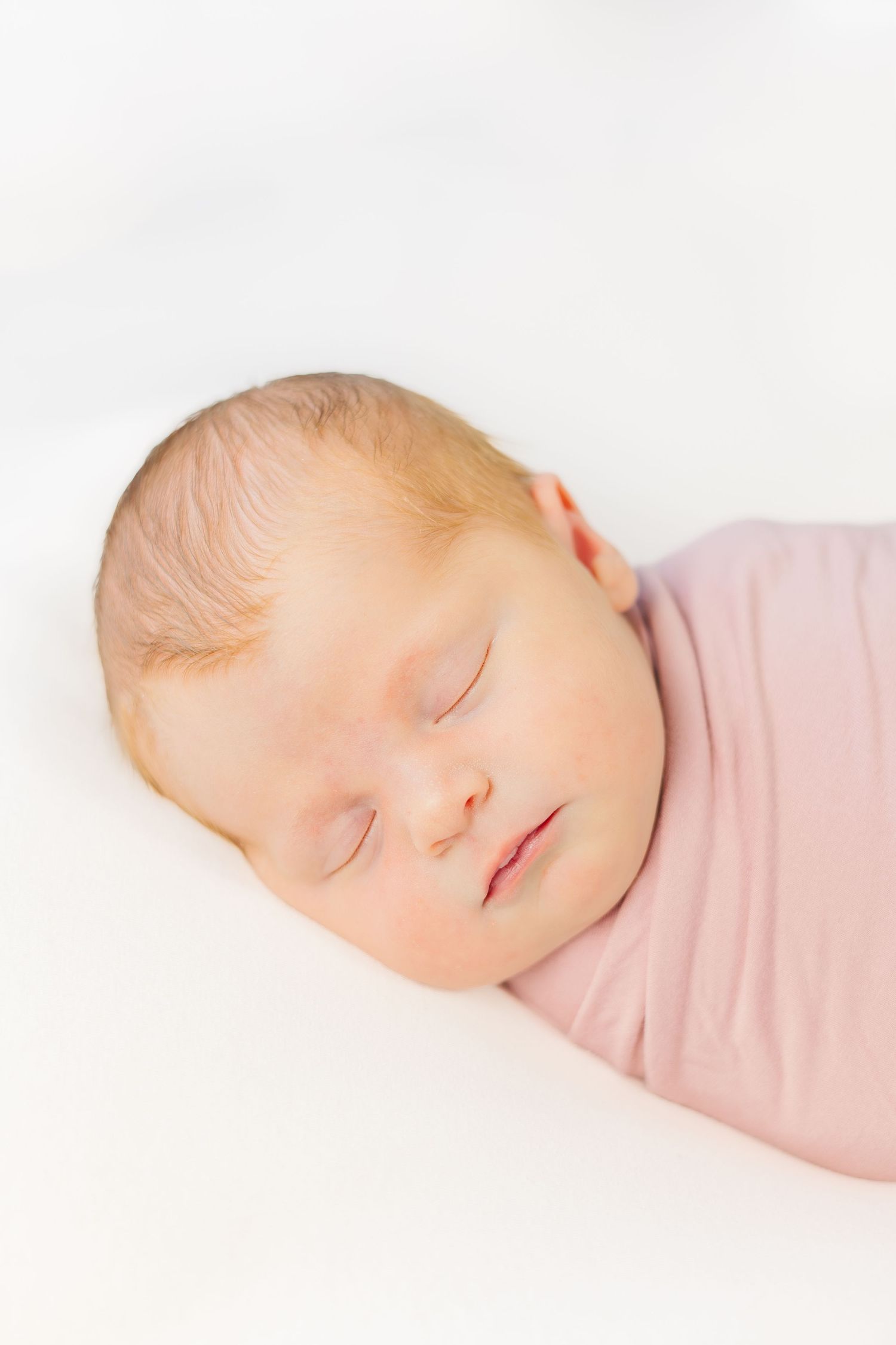 Peaceful sleeping newborn wrapped in pink swaddle against white background.