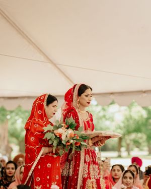 Wedding ceremony participants in red traditional attire hold ceremonial items during the ritual.