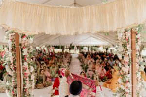 Wedding ceremony tent decorated with white drapes and floral garlands overlooking seated guests.