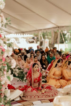 Traditional wedding ceremony with red bridal attire and floral decorations under white tent.